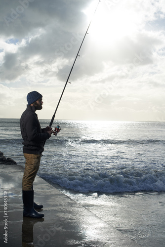 Thinking, fishing and man at a beach with pole for water hobby, recreation or stress relief vacation in nature. Casting, rod and fisherman at sea for travel, adventure or fisher sports in Cape Town