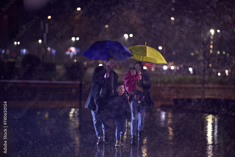 In the midst of a rainy urban night, a happy couple takes their children on a stroll through the city streets, heading towards the cinema for a delightful family movie outing