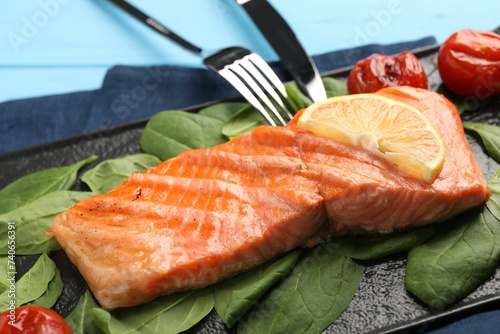Tasty grilled salmon with tomatoes, spinach and lemon served on table, closeup