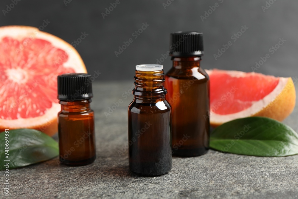 Grapefruit essential oil in bottles, leaves and fruit on dark textured table, closeup Grapefruit essential oil in bottles, leaves and fruit on dark textured table, closeup