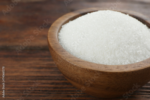 Granulated sugar in bowl on wooden table, closeup. Space for text