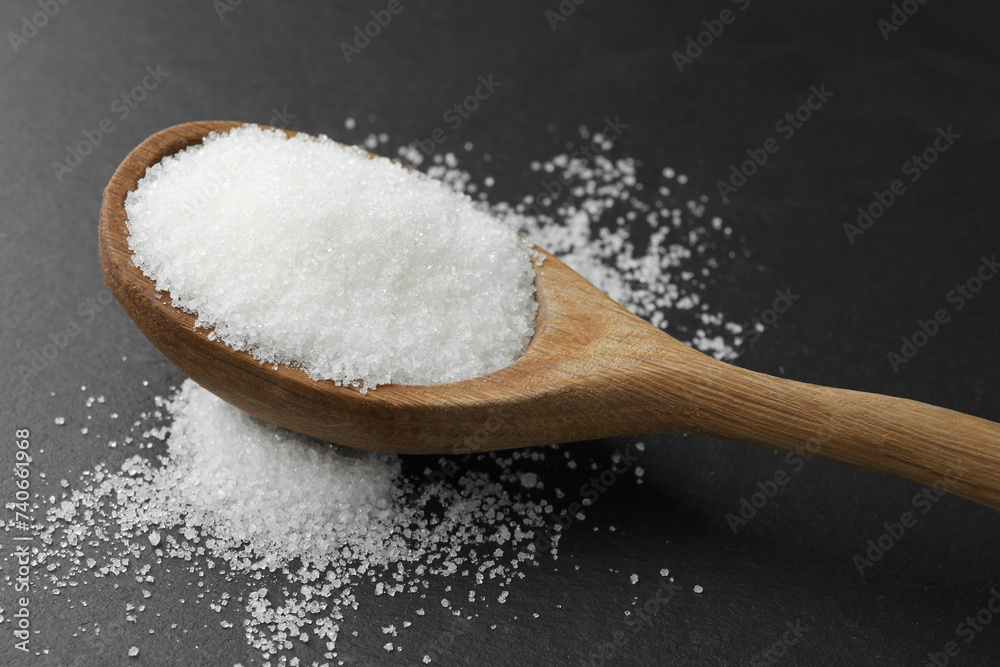 Spoon with granulated sugar on black table, closeup Spoon with granulated sugar on black table, closeup