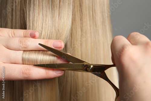 Hairdresser cutting client s hair with scissors on light grey background  closeup