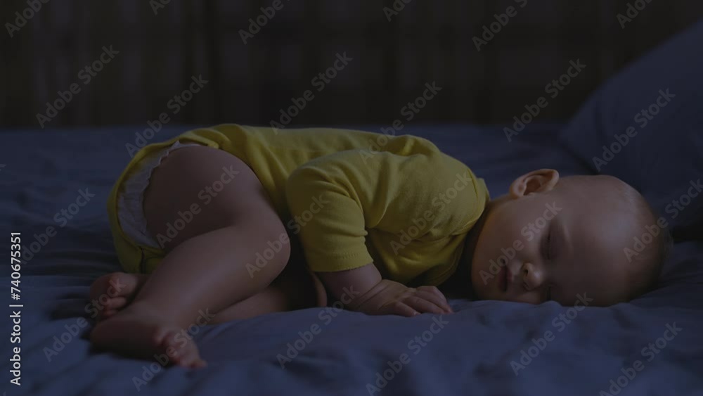Cute Infant curl in rest sleep, wear yellow, on dark blue bedding, dimly lit room evoke a serene nocturnal atmosphere. Baby boy in comfort slumber position, night time setting, tranquil environment.