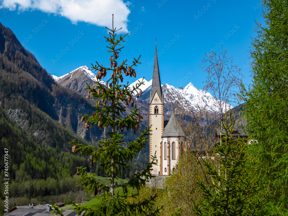 Scenic view on church Hl Vinzenz in Heiligenblut on Grossglockner high alpine road, Carinthia Salzburg, Austria. Landmark is surrounded by steep snow covered mountain peaks. Tranquility Austrian Alps