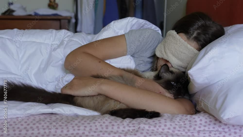 A fluffy cat wakes up a sleeping woman in the morning, a blonde woman sleeps with an eye mask on her head. A fluffy cat wakes up a sleeping woman in the morning, a blonde woman sleeps with an eye mask on her head.