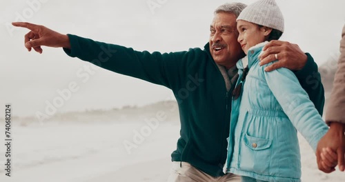 Grandfather, beach and child with point, holiday and happy for teaching in nature, bonding or holding hands. People, family and kid with senior man, hug or show direction by sea on vacation with chat photo