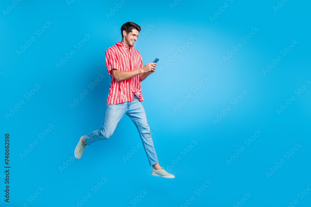 Full body photo of busy guy wear stylish shirt jeans trousers run empty space read sms on smartphone isolated on blue color background Full body photo of busy guy wear stylish shirt jeans trousers run empty space read sms on smartphone isolated on blue color background