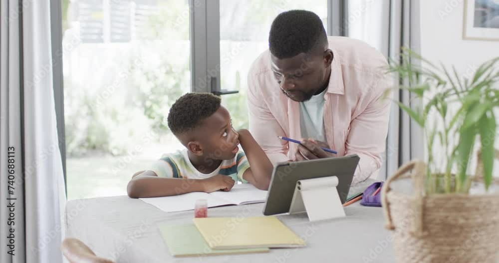 African American man helps a boy with homework at home using a tablet African American man helps a boy with homework at home using a tablet