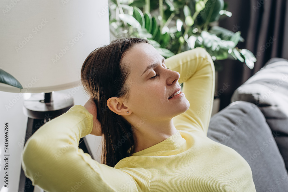 Close up of smiling peaceful young woman with closed eyes relaxing on comfy sofa at home, calm mindful female leaning back, visualizing good future, taking nap or daydreaming, enjoying leisure time Close up of smiling peaceful young woman with closed eyes relaxing on comfy sofa at home, calm mindful female leaning back, visualizing good future, taking nap or daydreaming, enjoying leisure time