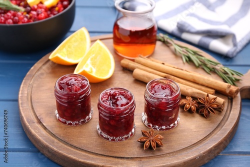 Cranberry sauce in jars and ingredients on blue wooden table, closeup