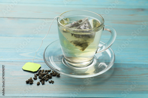Tea bag in cup with hot drink and dry leaves on light blue wooden table