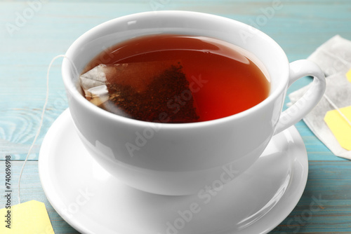 Tea bag in cup with hot drink on light blue wooden table, closeup