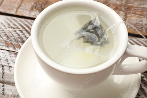 Tea bag in cup with hot water on wooden rustic table, closeup