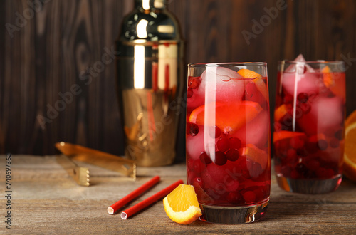 Tasty cranberry cocktail with ice cubes and orange in glasses on wooden table, space for text