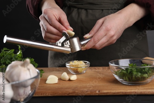 Woman squeezing garlic with press at black table, closeup photo