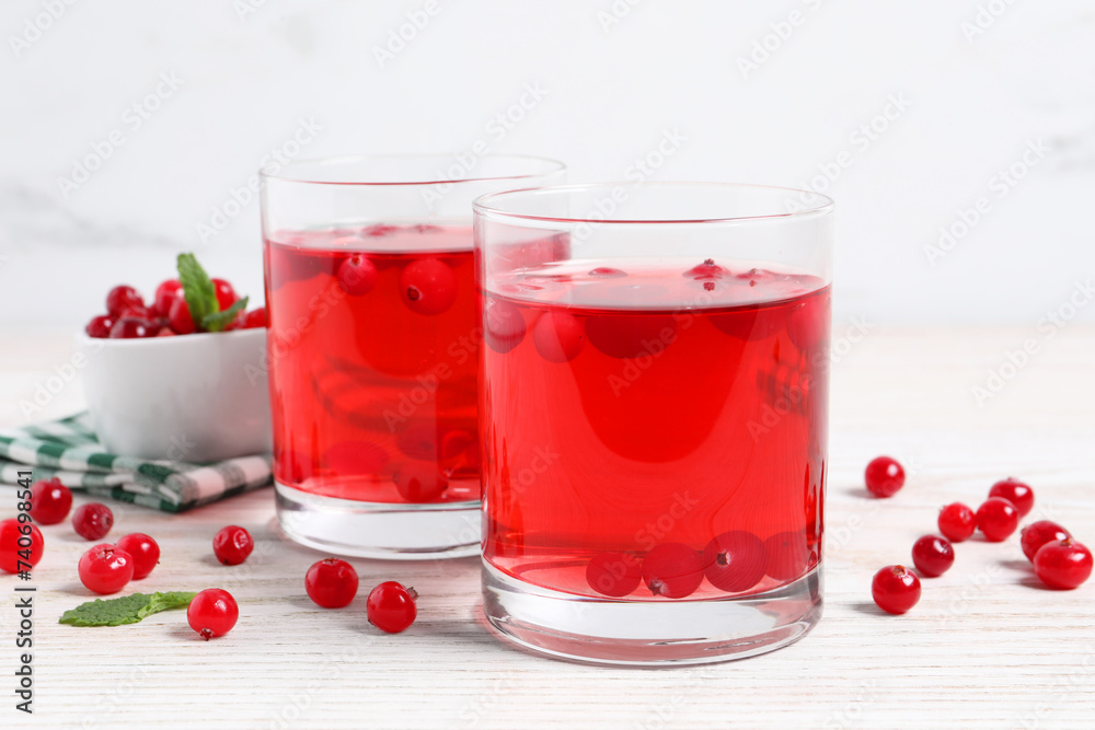 Tasty cranberry juice in glasses and fresh berries on white wooden table Tasty cranberry juice in glasses and fresh berries on white wooden table