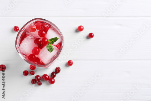Tasty cranberry juice with ice cubes in glass and fresh berries on white wooden table, flat lay. Space for text