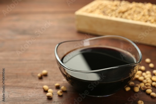 Soy sauce in bowl and soybeans on wooden table, closeup. Space for text
