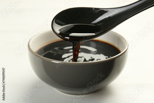 Taking soy sauce with spoon from bowl at white table, closeup