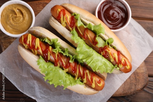 Tasty hot dogs with lettuce, ketchup and mustard on wooden table, top view
