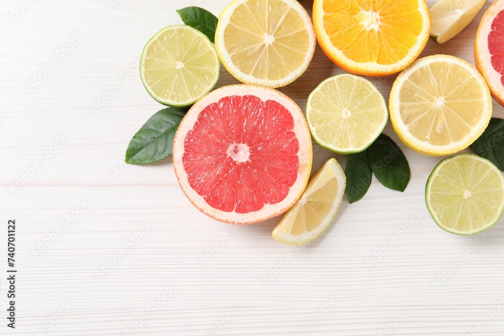 Different cut citrus fruits and leaves on white wooden table, flat lay. Space for text Different cut citrus fruits and leaves on white wooden table, flat lay. Space for text