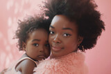 joven madre afroamericana sosteniendo a su hija en brazos mirando a cámara sonrientes, llevando vestidos rosas, sobre fondo rosa con efecto bokeh
