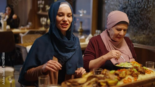 Muslim Mother and Daughter Having Dinner and Talking in a Restaurant in Ramadan or on Eid photo