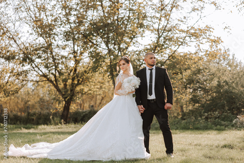 Wedding couple on a walk in the autumn park. The bride in a beautiful white dress. Love and relationship concept. Groom and bride in nature outdoors