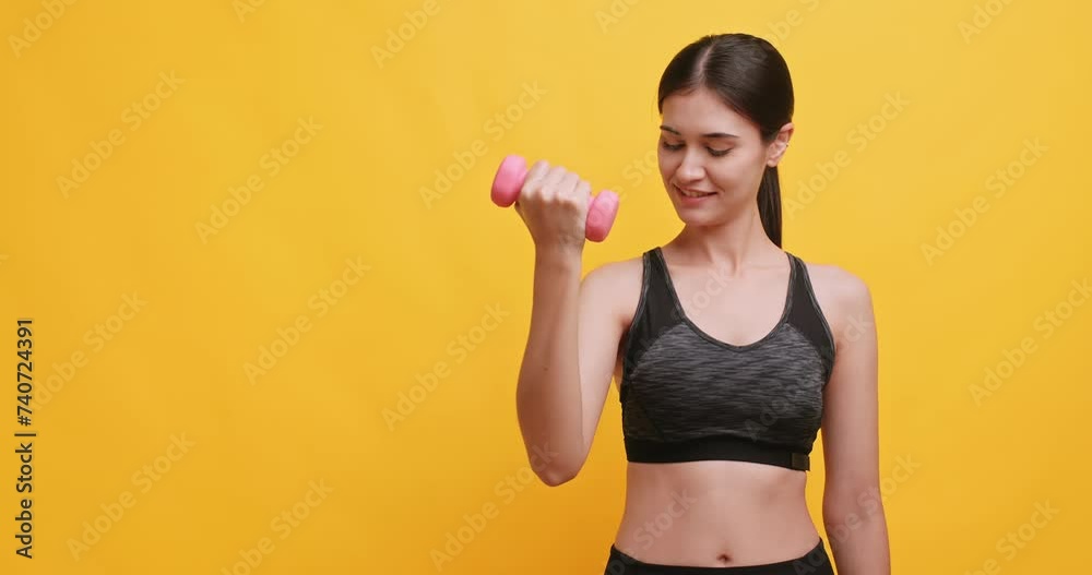 Young sportswoman shows off her physical strength by lifting dumbbells. Isolated on yellow background in studio. Young sportswoman shows off her physical strength by lifting dumbbells. Isolated on yellow background in studio.