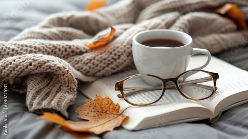 Cozy hygge concept with beige sweater, tea or coffee mug, book, and glasses on gray bed.