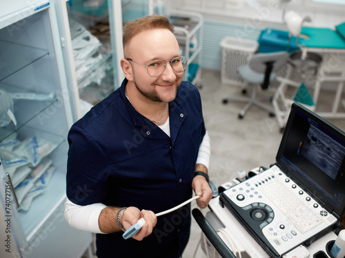 Portrait of a sonographer working on a modern ultrasound machine in a clinic. Professional smiling modern adult ultrasound medicine doctor photo