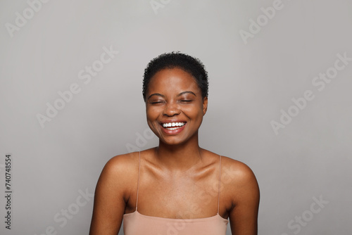 Laughing healthy young woman with dark shiny skin smiling looking at camera on white background. Cosmetology, skincare, facial treatment concept