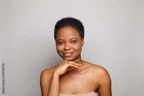 Cute healthy young woman with dark shiny skin smiling looking at camera on white background. Cosmetology, skincare, facial treatment concept