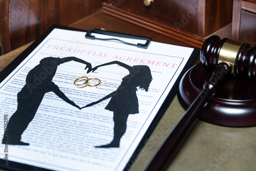 A clipboard holding a prenuptial agreement with a cut-out silhouette of a couple and wedding rings, next to a judge's gavel. photo