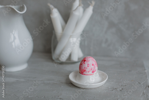 A painted Easter egg on a stand, candles in a glass vase, a jug on the mantelpiece. Minimalistic still life in gray.