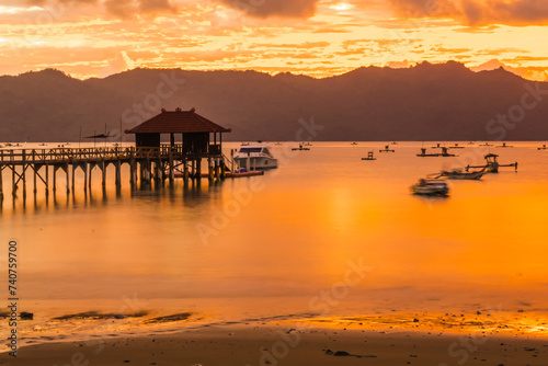 A wooden pier stretches out into a calm bay at sunset, with mountains in the background. photo