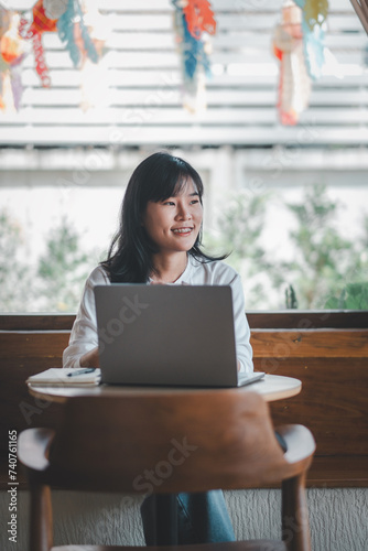 Freelance concept, A smiling woman is working on her laptop in a cafe decorated with colorful paper lanterns, enjoying a bright day.