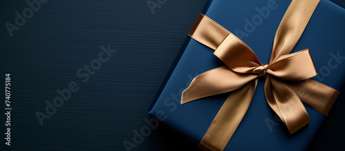 Dark blue christmas gift box with gold satin ribbon on dark background. Top view of birthday gift with copy space