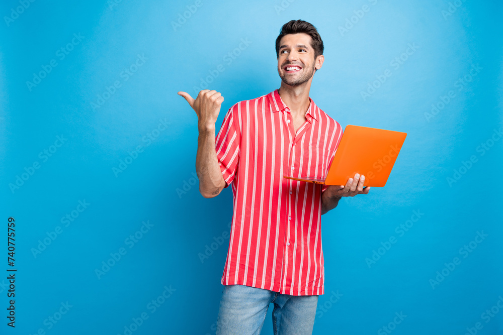 Photo of funky dreamy man dressed striped shirt communicating modern device thumb empty space isolated blue color background Photo of funky dreamy man dressed striped shirt communicating modern device thumb empty space isolated blue color background