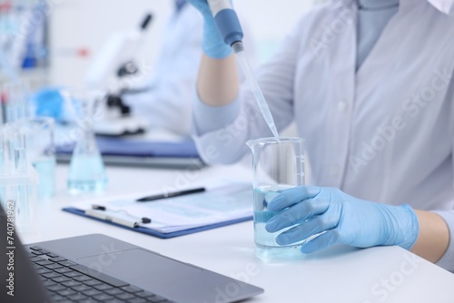 Scientist dripping sample into beaker in laboratory, closeup