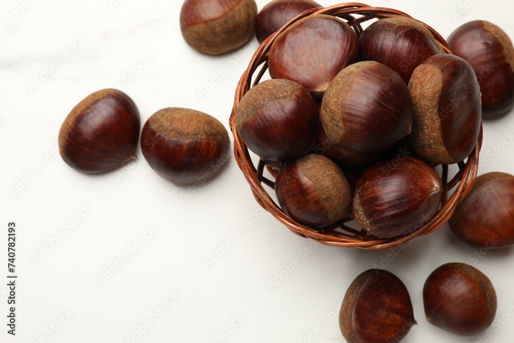 Sweet fresh edible chestnuts in wicker bowl on white table, top view. Space for text Sweet fresh edible chestnuts in wicker bowl on white table, top view. Space for text