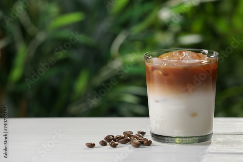 Glass of iced coffee and beans on white wooden table outdoors. Space for text