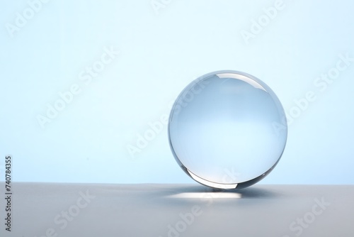 Transparent glass ball on table against light blue background. Space for text