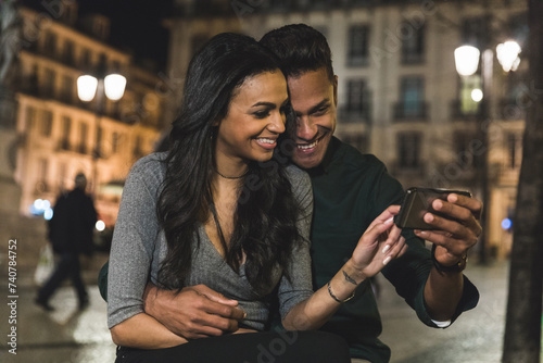 Happy multiracial couple sharing a moment with smartphone at night