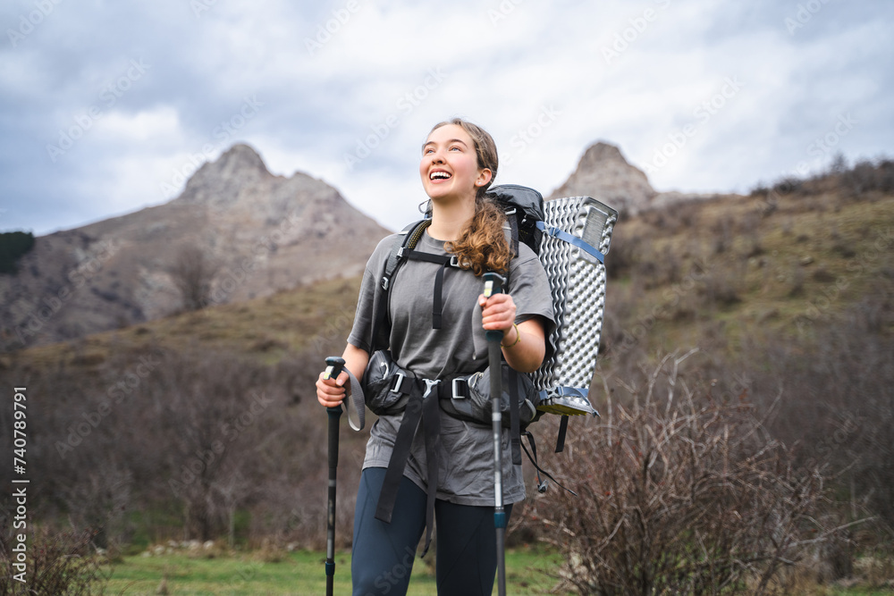 Portrait of smiling happy young woman wearing hiking clothes, traveler on the way is filled with emotions and admires the beauty of the landscapes, hiker looking up and enjoying the fascinating view