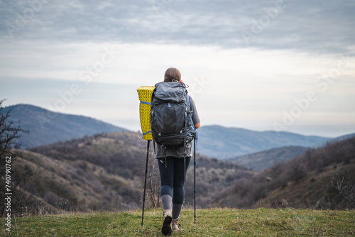 Back view of young backpacker woman with backpack on travel and enjoying mountains landscape, tourist in hiking equipment looks into distance at peaks of mount on a cloudy day, summer vacation journey © Соня Монштейн
