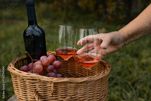 One glass of tasty dry rose wine from ripe grapes with a bottle of wine on a wicker basket in the vineyard on grape plantation background. Take glass of wine. 