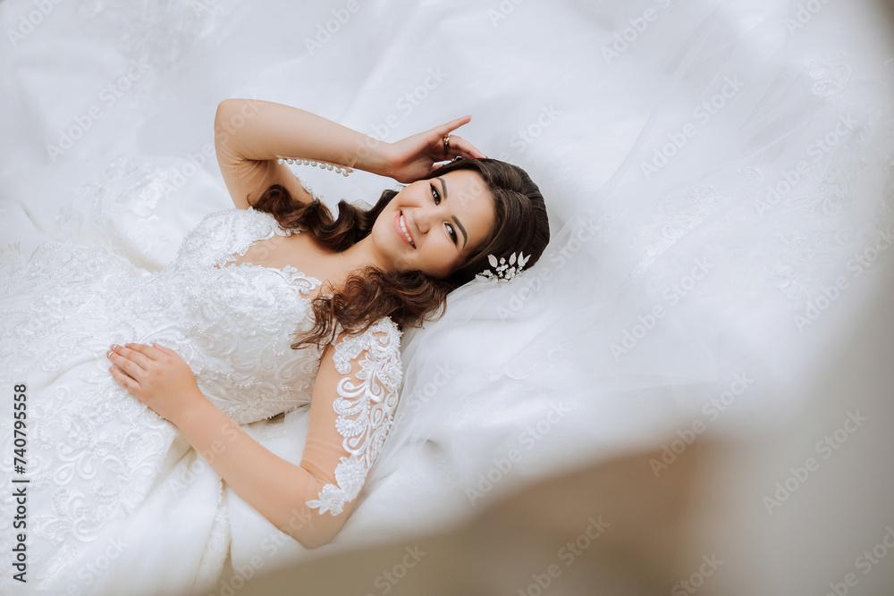 A brunette bride is lying on a lace dress and tiara, posing touching her hair A brunette bride is lying on a lace dress and tiara, posing touching her hair