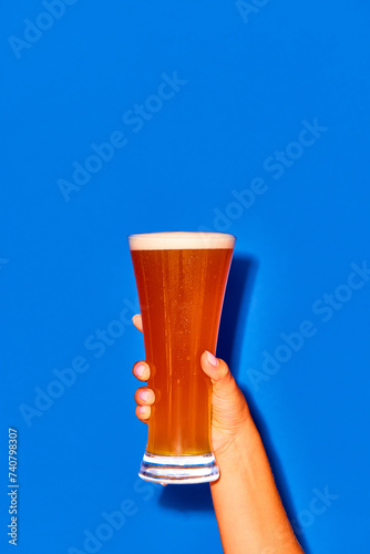 Woman holding long glass with fresh beer isolated on blue background. Chill drops falling down. Concept of alcohol drink, brewery, Oktoberfest, holidays, festival. Poster. Copy space for ad